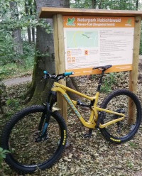 Ein senfgelbes Mountainbike steht vor der Infotafel des Trailparks Hohes Gras in Kassel.